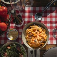 Fresh tomatoes and a pan of pasta on a red check tablecloth